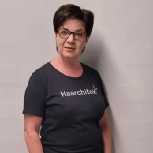 Frau mit kurzen dunklen Haaren und Brille, die ein Haarchitek-T-Shirt trägt.